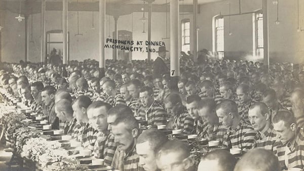 A black and white photo of men sitting at rows in tables
