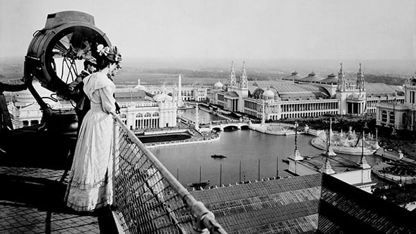 A man and woman look out over a lagoon and grand buildings in the "White City" of Chicago's 1893 World's Fair