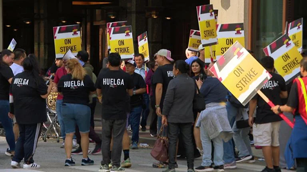 A group of hotel workers wearing black t-shirts and carrying signs that say "ON STRIKE"