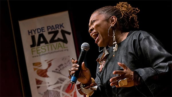 Dee Alexander holds a microphone and sings in front of a banner that reads Hyde Park Jazz Festival