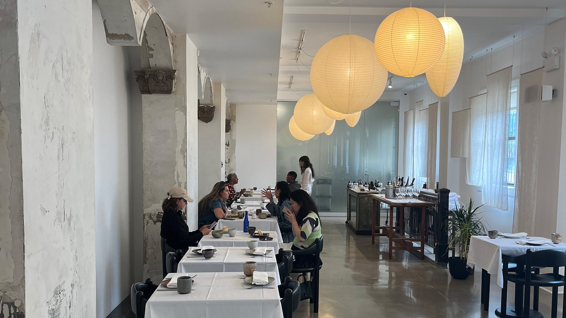 People sit at tables in a white room with paper lanterns