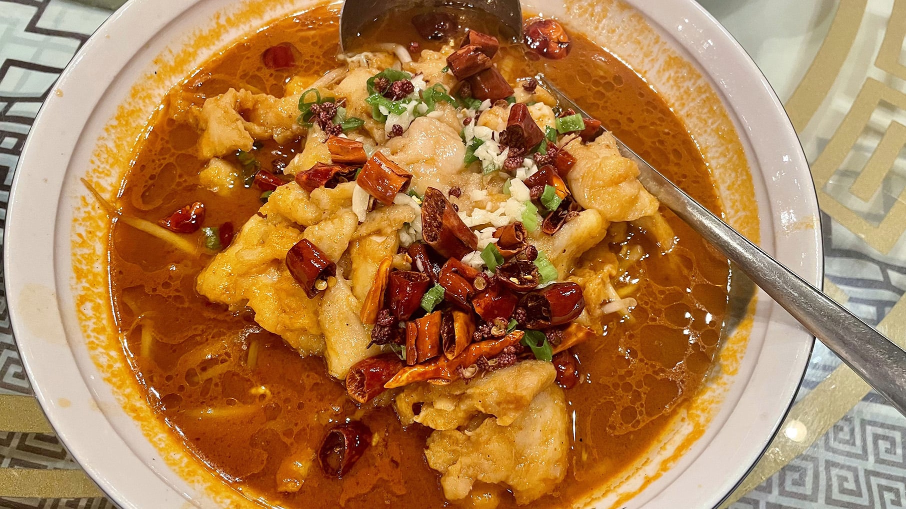 A bowl of fish topped with chiles and scallions in a red sauce