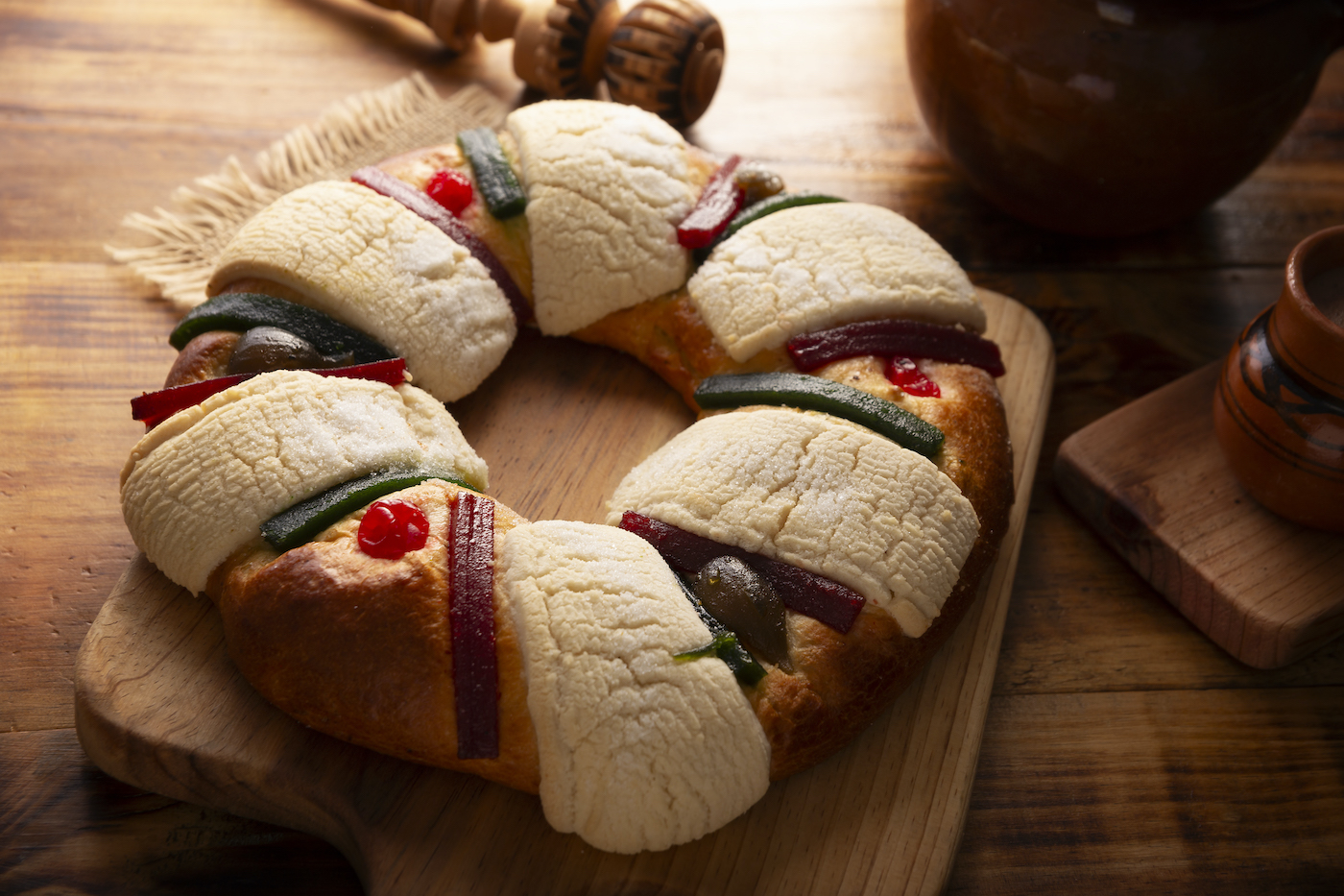 Rosca de reyes on a wooden cutting board next to a ceramic mug of atole
