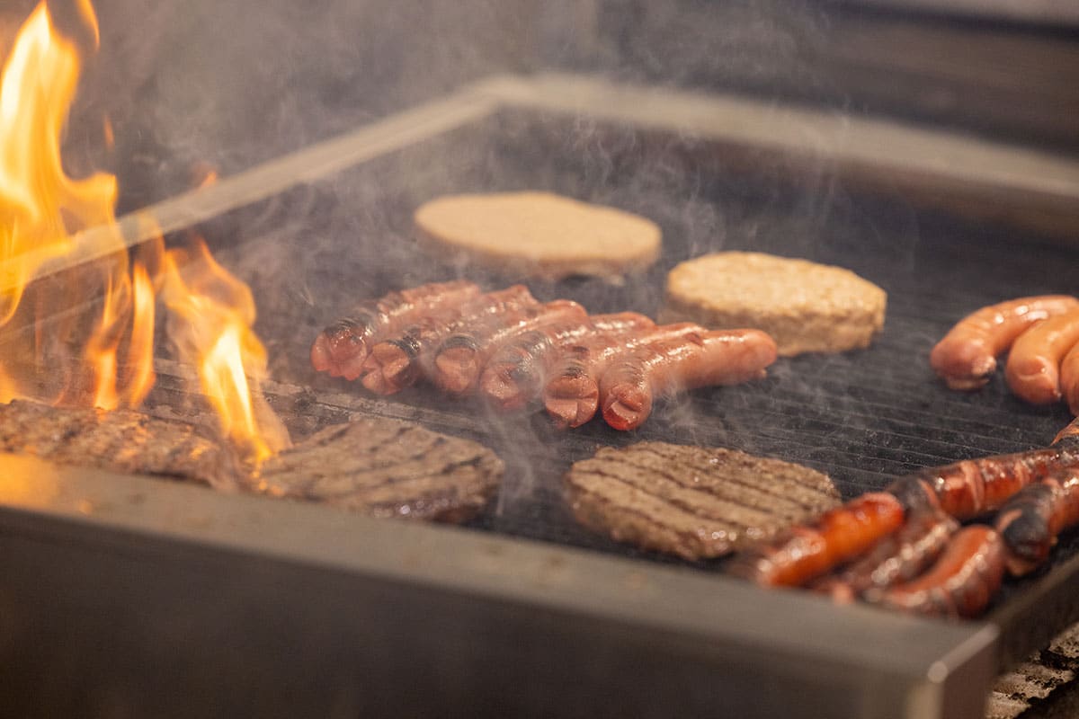 Hamburgers and hot dogs being cooked on a flaming grill.