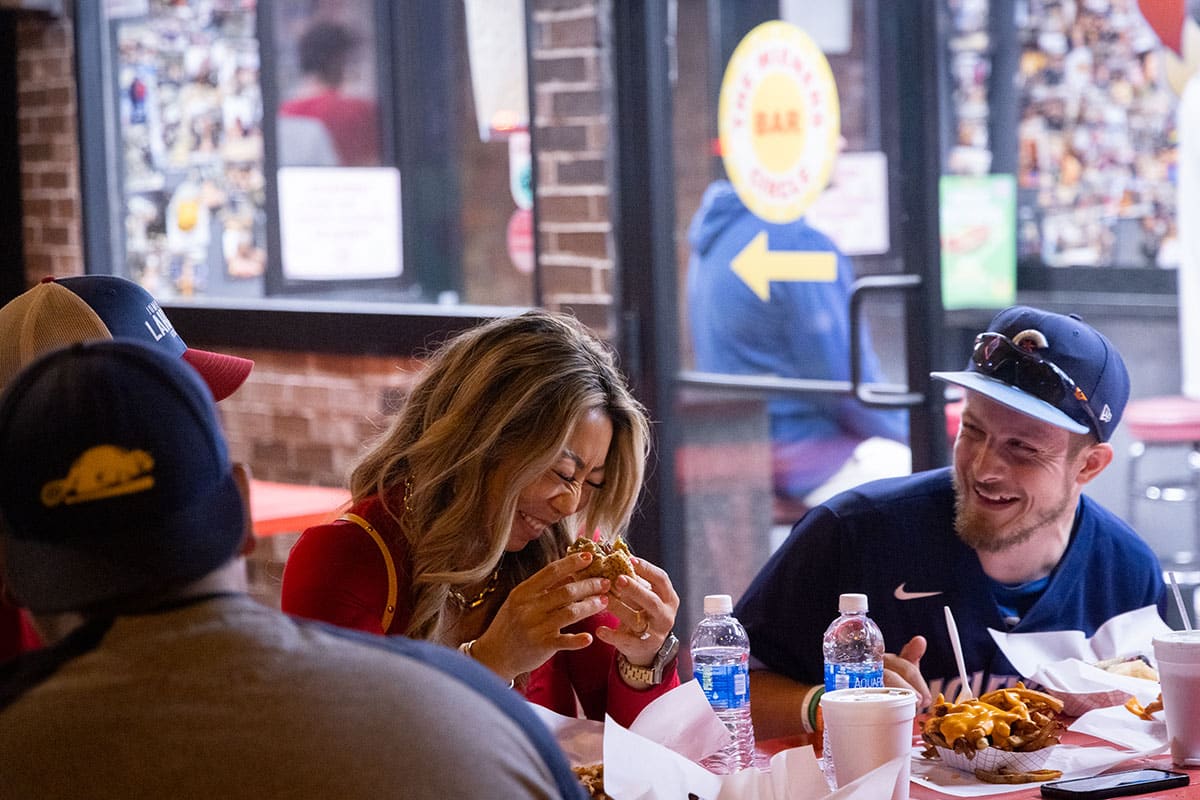 A woman and man laugh while eating their food at a picnic table