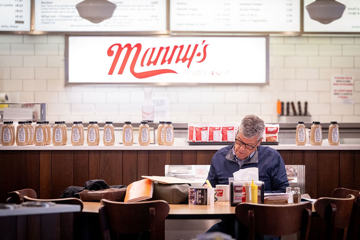 A man sits at a table in a diner, focused on reading, with retro decor in the background.