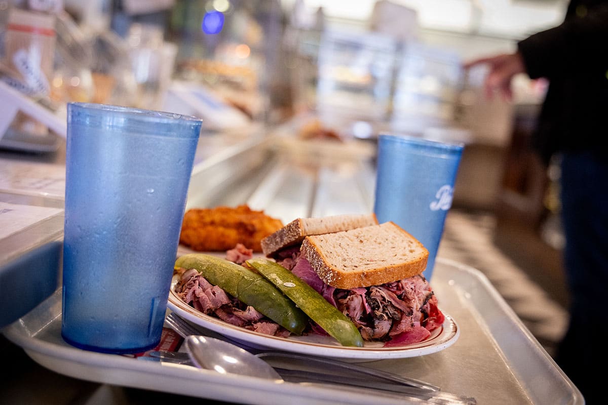 A plate with a sandwich, pickles, a side of fried food, and blue cups on a tray.