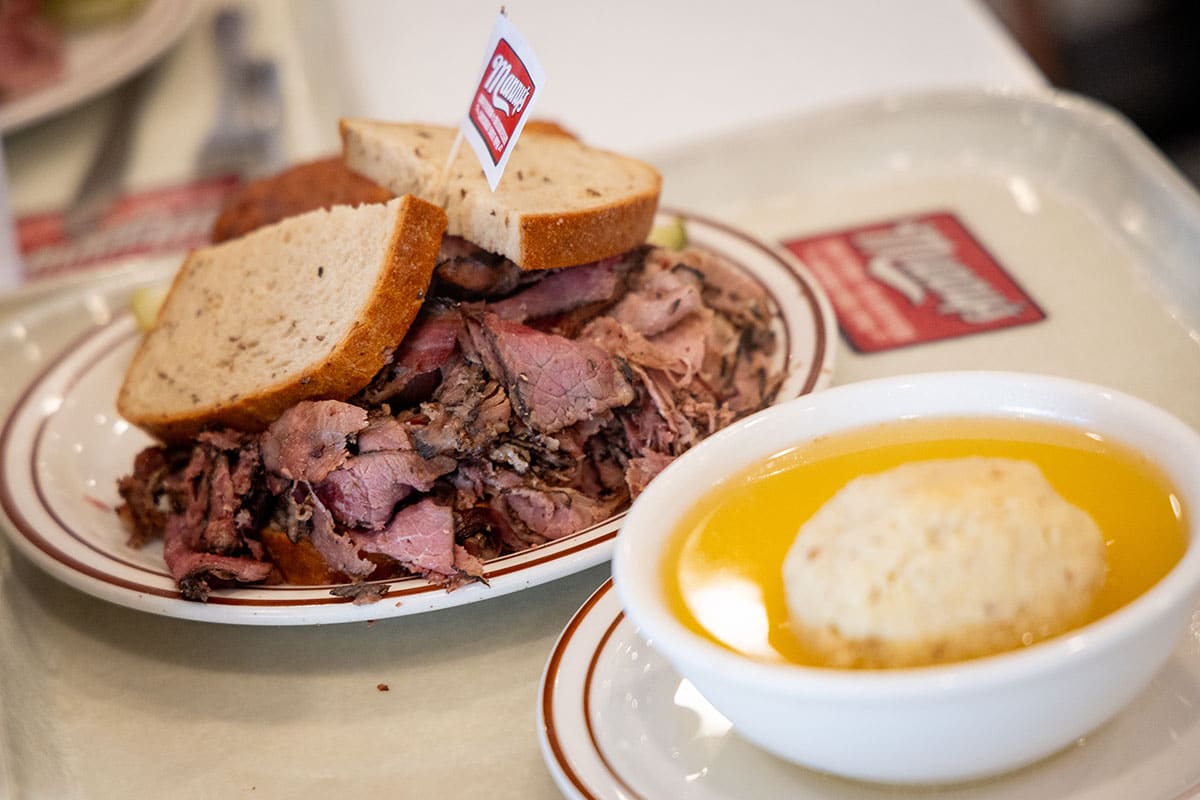 Plate of sliced pastrami with bread and a bowl of matzo ball soup on a tray.