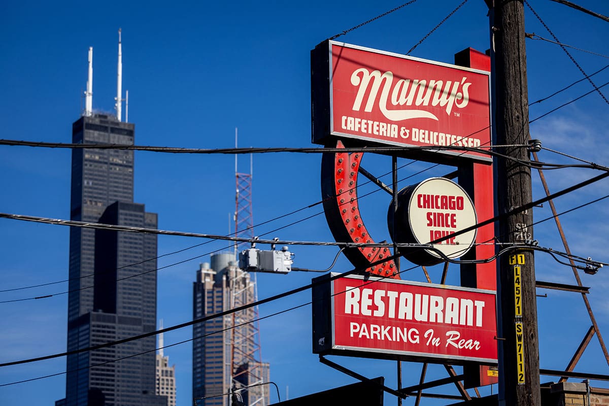 Manny's Restaurant sign with skyscrapers in the background against a blue sky.