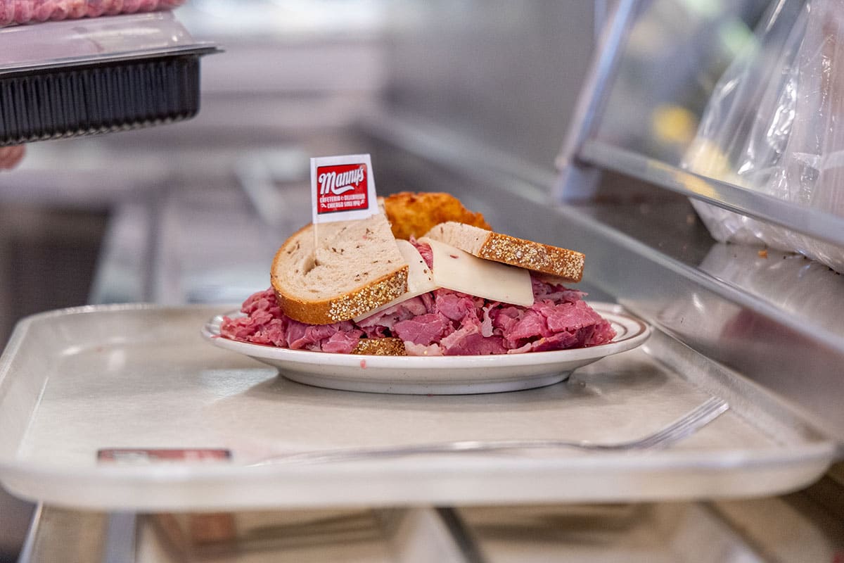 A plate with stacked corned beef, sliced bread, and a pickle, on a cafeteria tray.