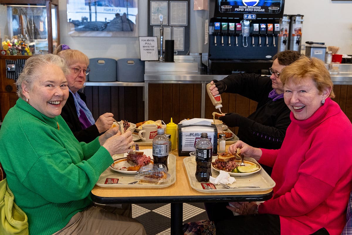 Four older adults enjoying a meal at a diner, smiling and chatting at a table.