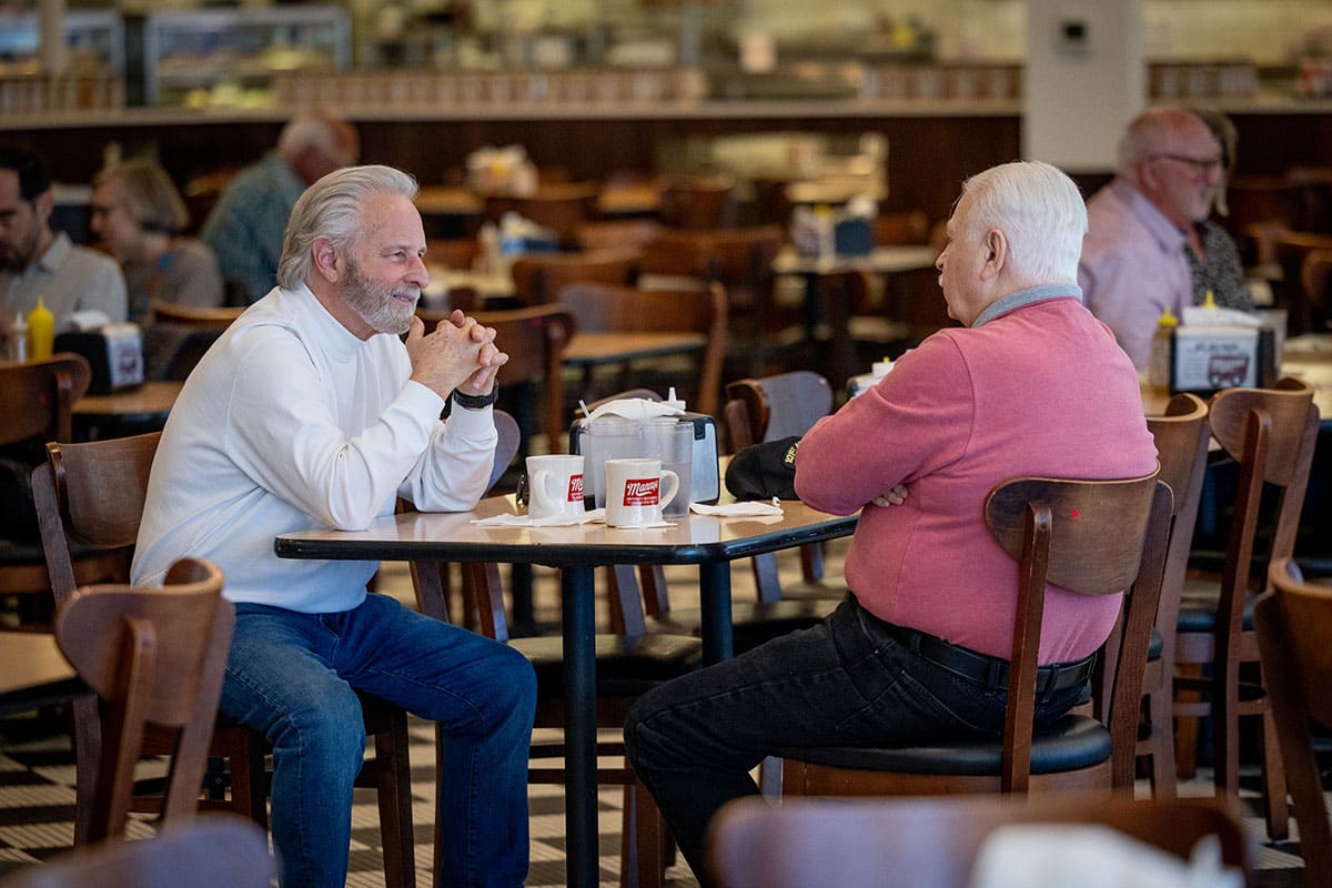 Two older men sitting at a cafe table, engaging in conversation.