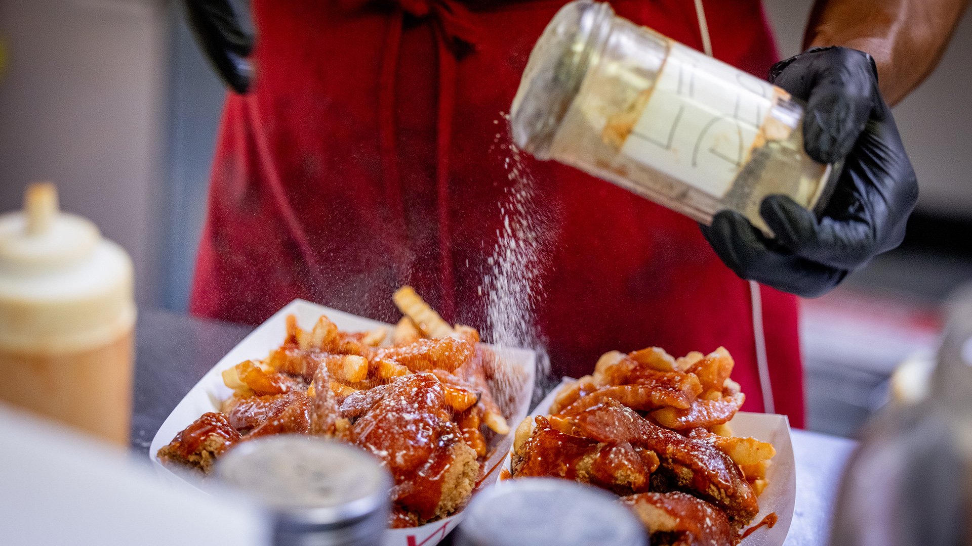 Lemon pepper being sprinkled over two orders of wings and fries