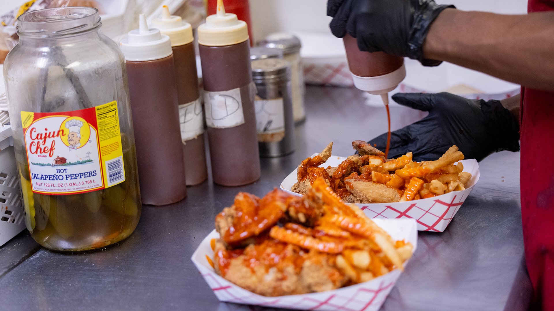 Mild sauce being drizzled over two orders of wings and fries