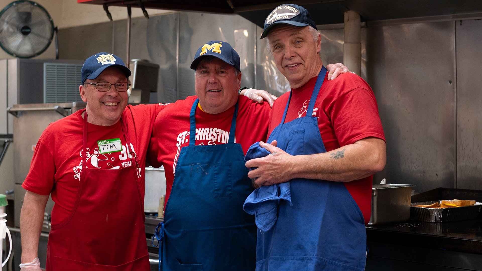 Three volunteers standing together in the kitchen smiling