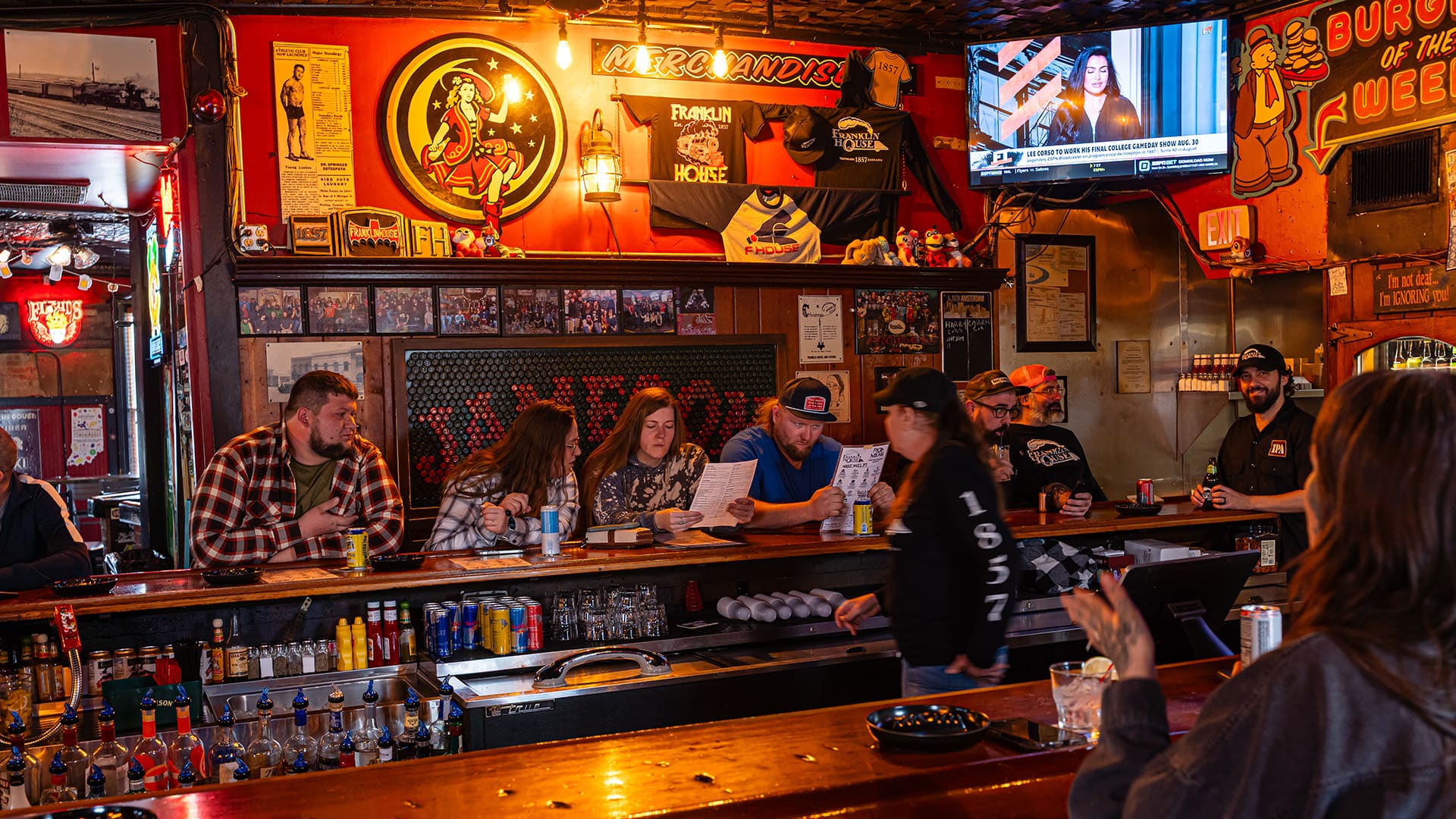 Patrons sit at the bar while the bartender pours a drink