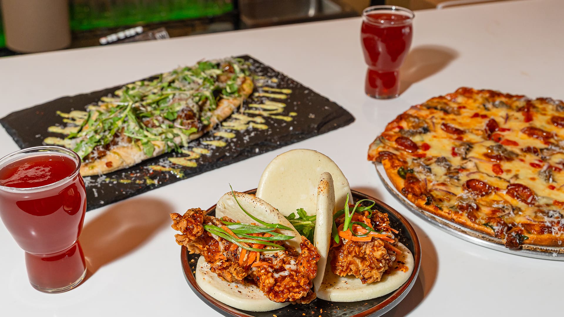 Beers, tacos, pizza and flatbread sit on a table