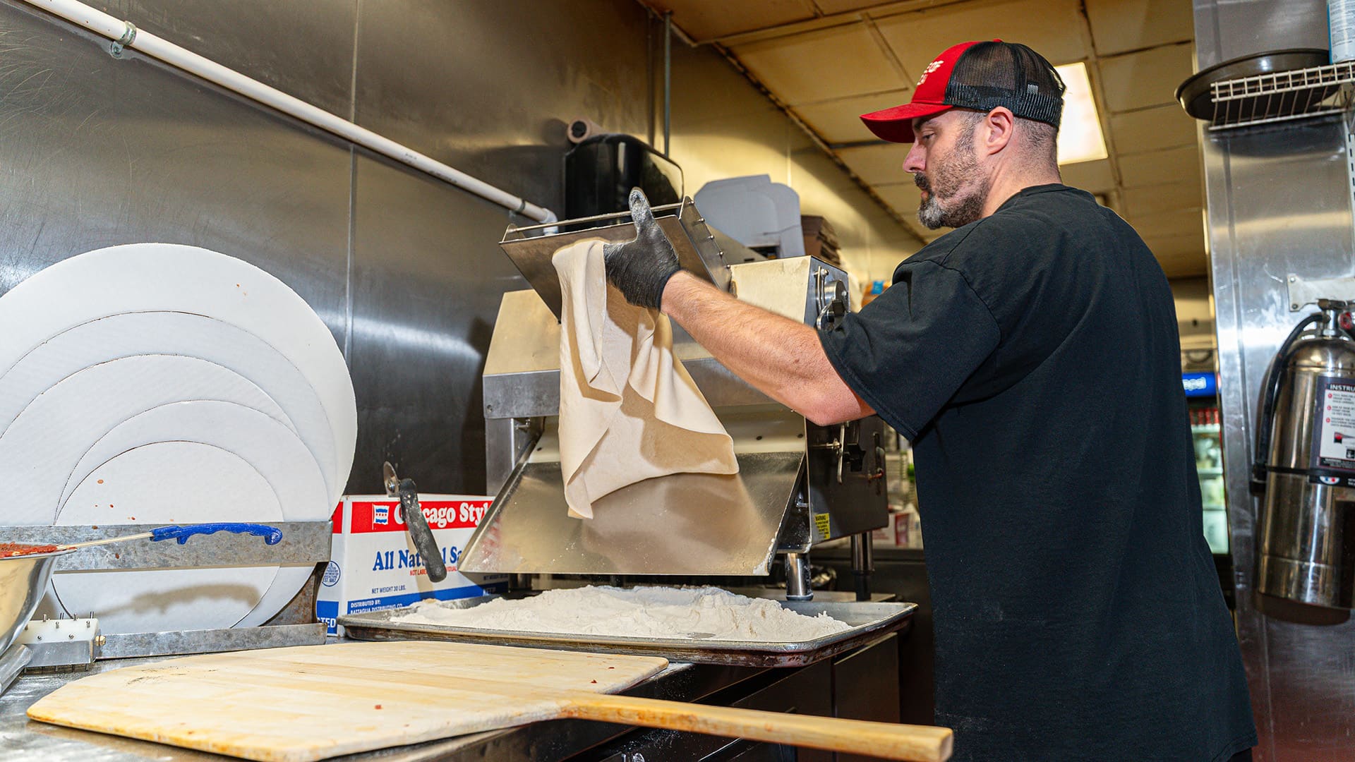 Danny running pizza dough through a machine to roll it