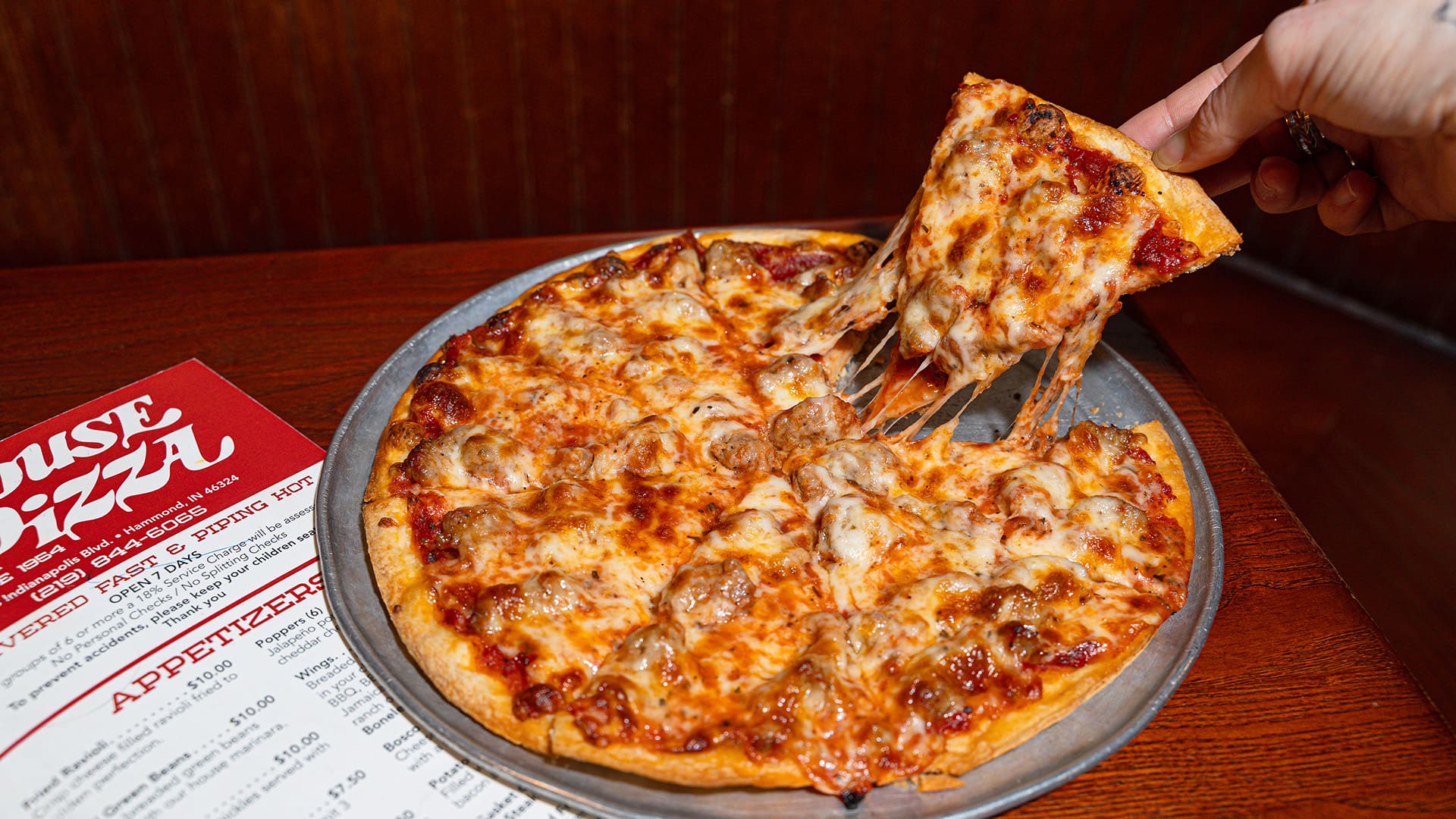 A triangle shaped slice of thin crust pizza being lifted with cheese stretching back to the rest of the pizza