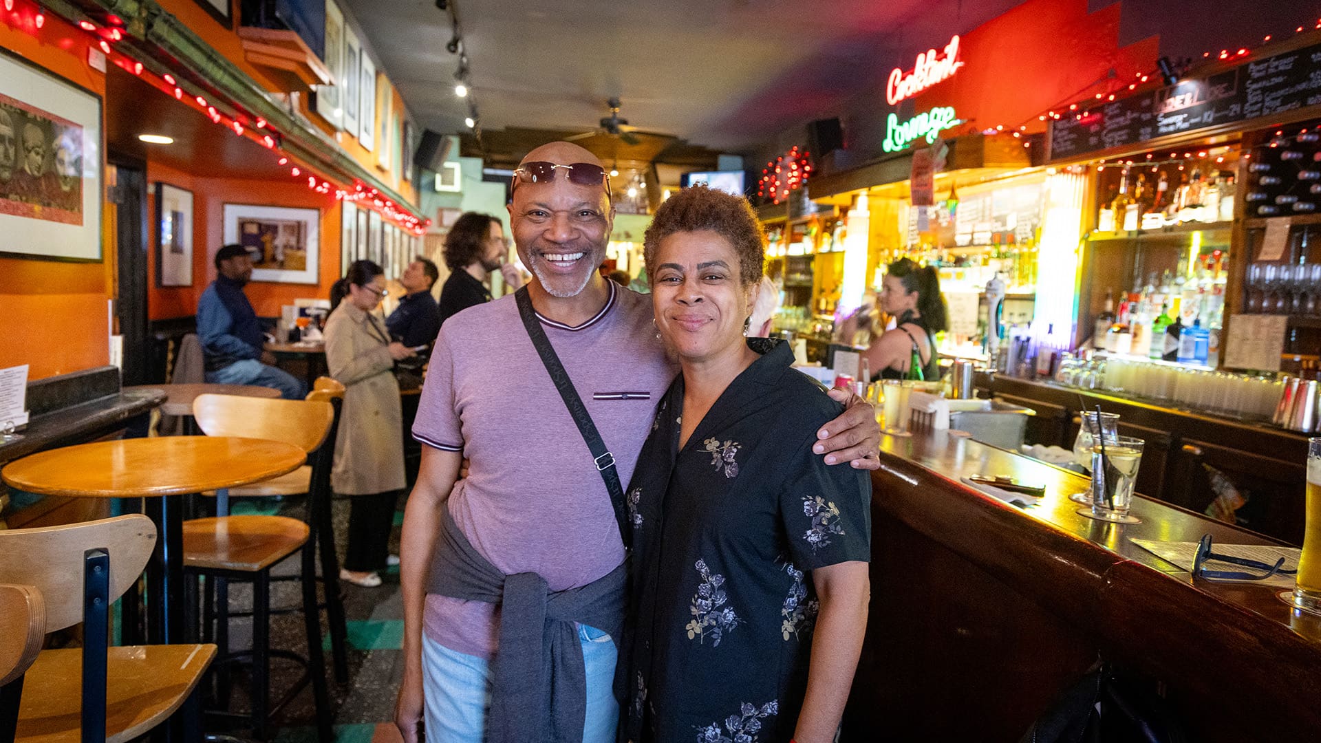 A man and woman pose in front of a bar, both smiling and enjoying their time together.