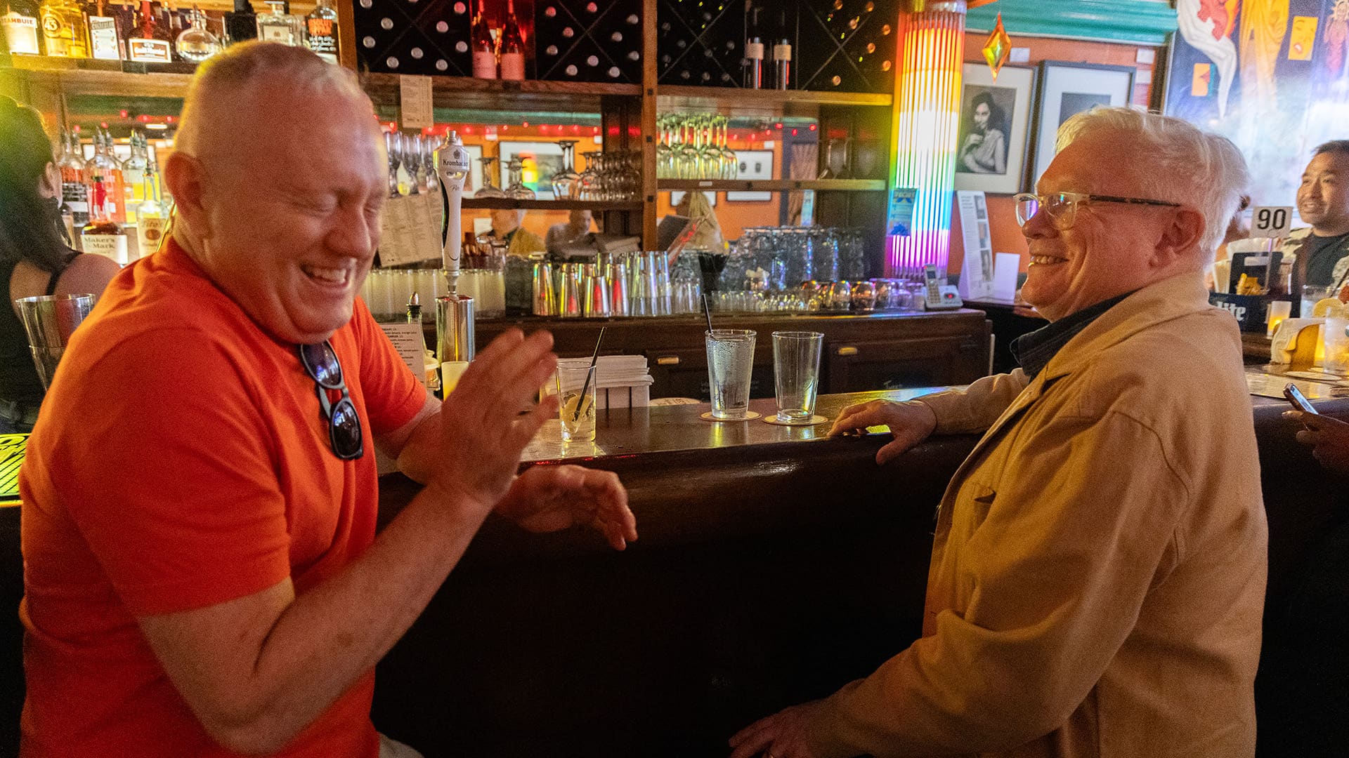 Two men sitting at a bar, engaged in conversation and sharing laughter.