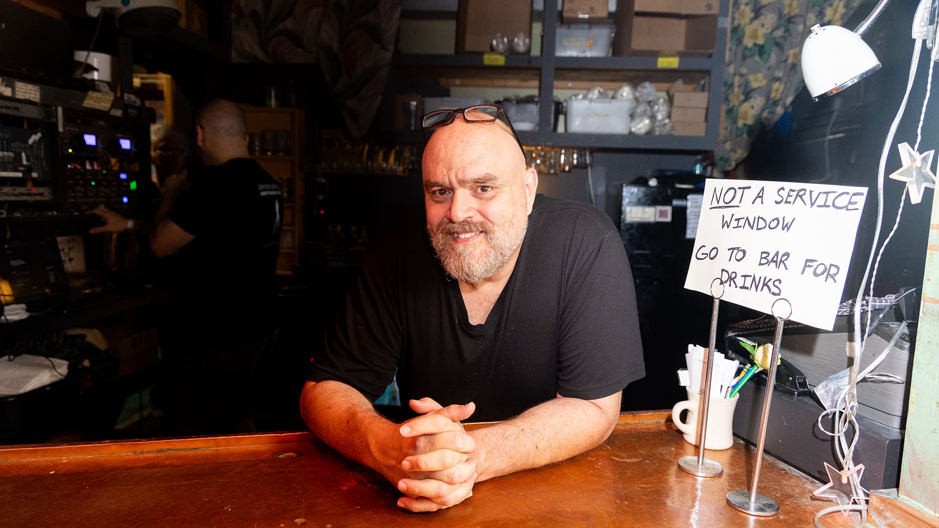 A man sitting behind a bar with a sign on the counter, indicating bar rules.