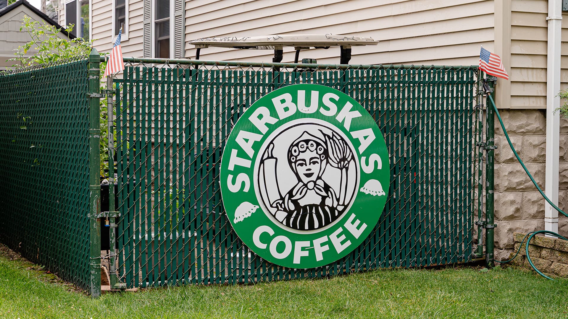 A 'Starbuskas Coffee' sign parodying the Starbucks Coffee design, is attached to a fence