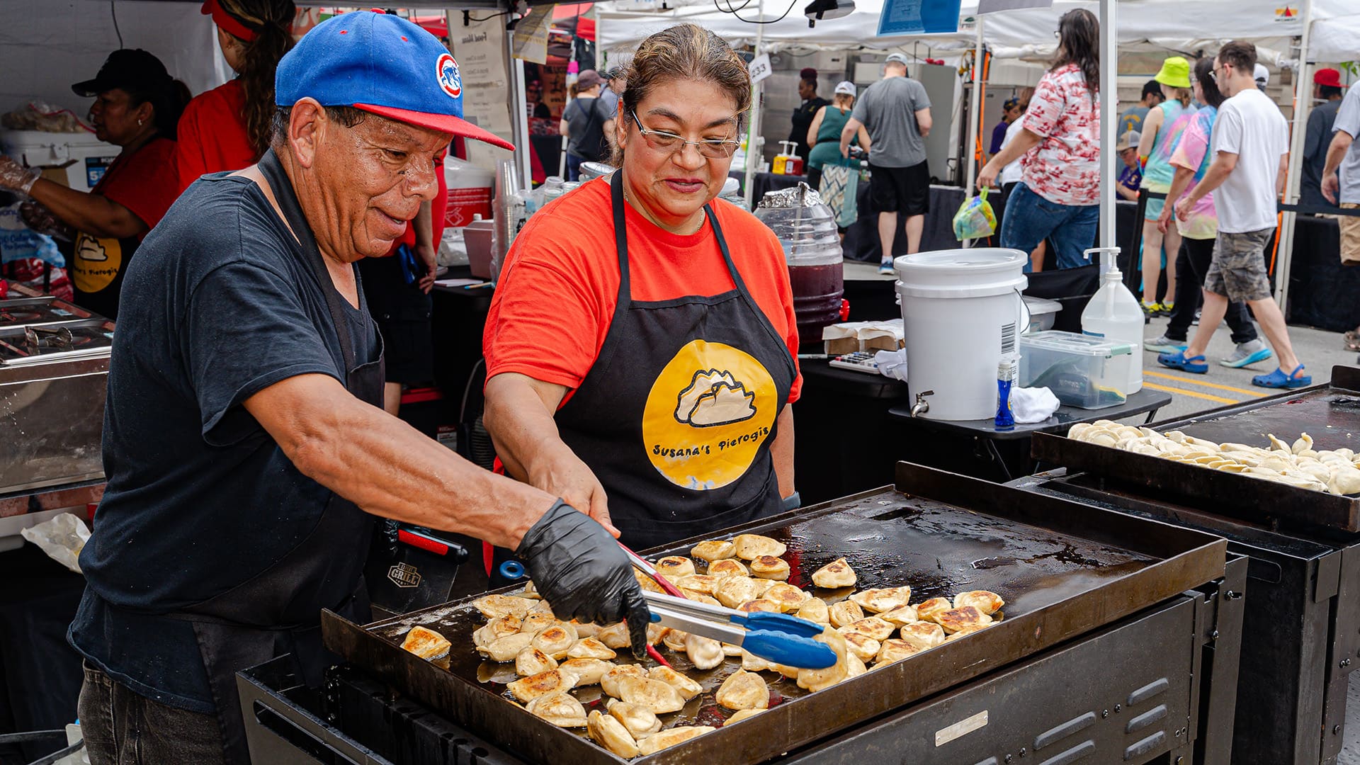 Two chefs turn pierogi on griddle to brown them