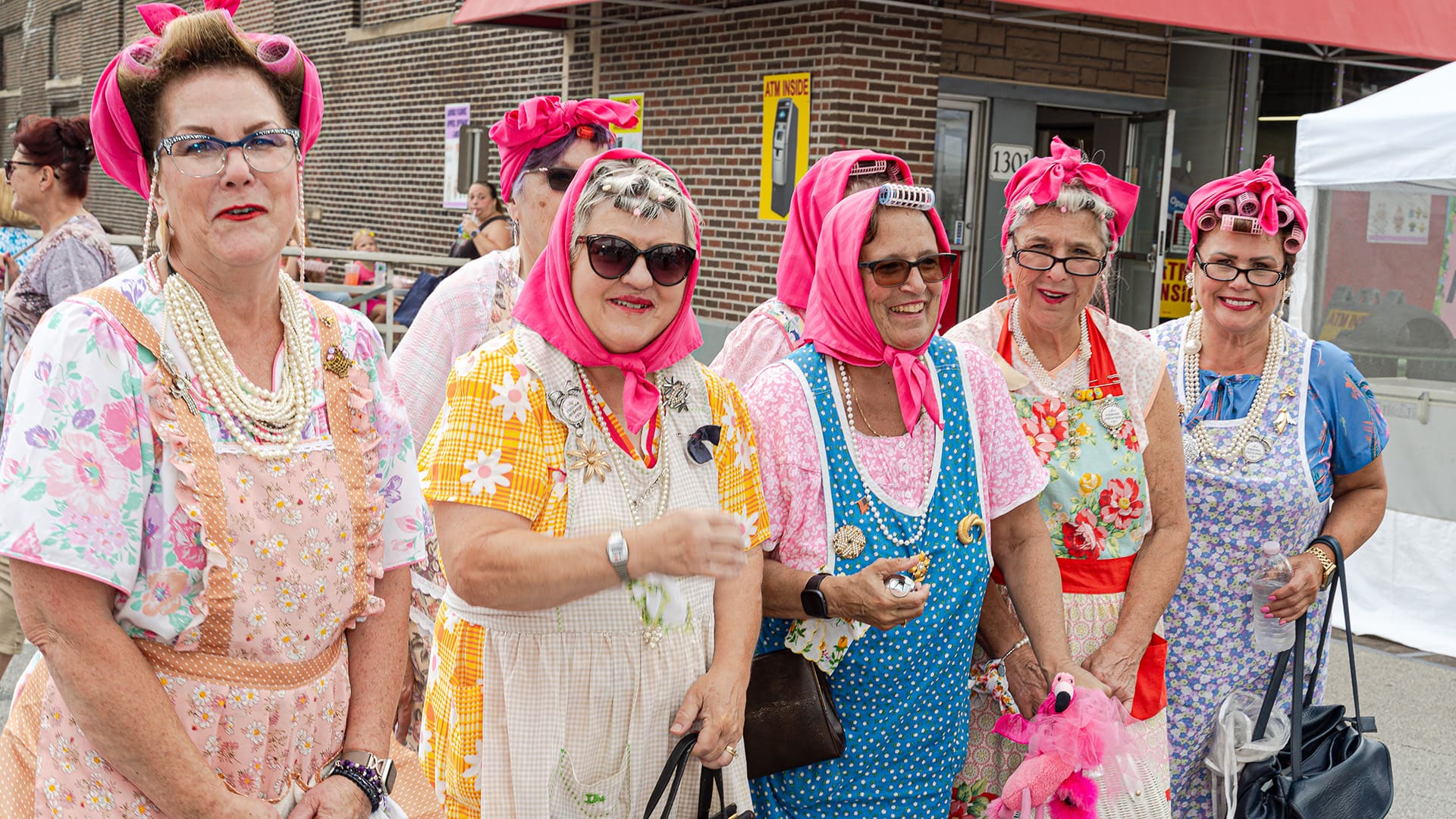Seven 'women' stand in dresses, aprons and pink headscarfs