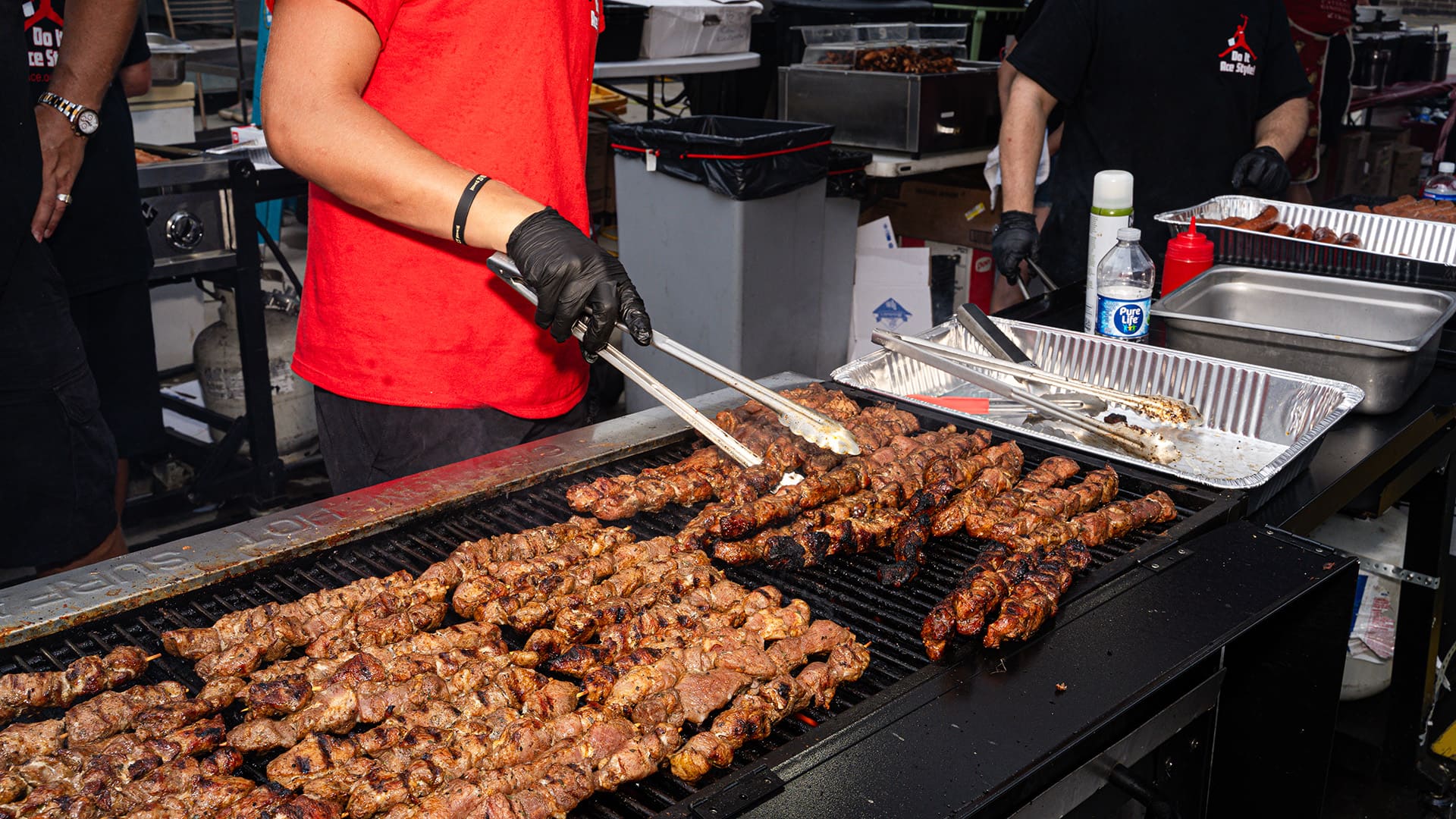 A worker using tongs turns shish-ka-bobs on the grill