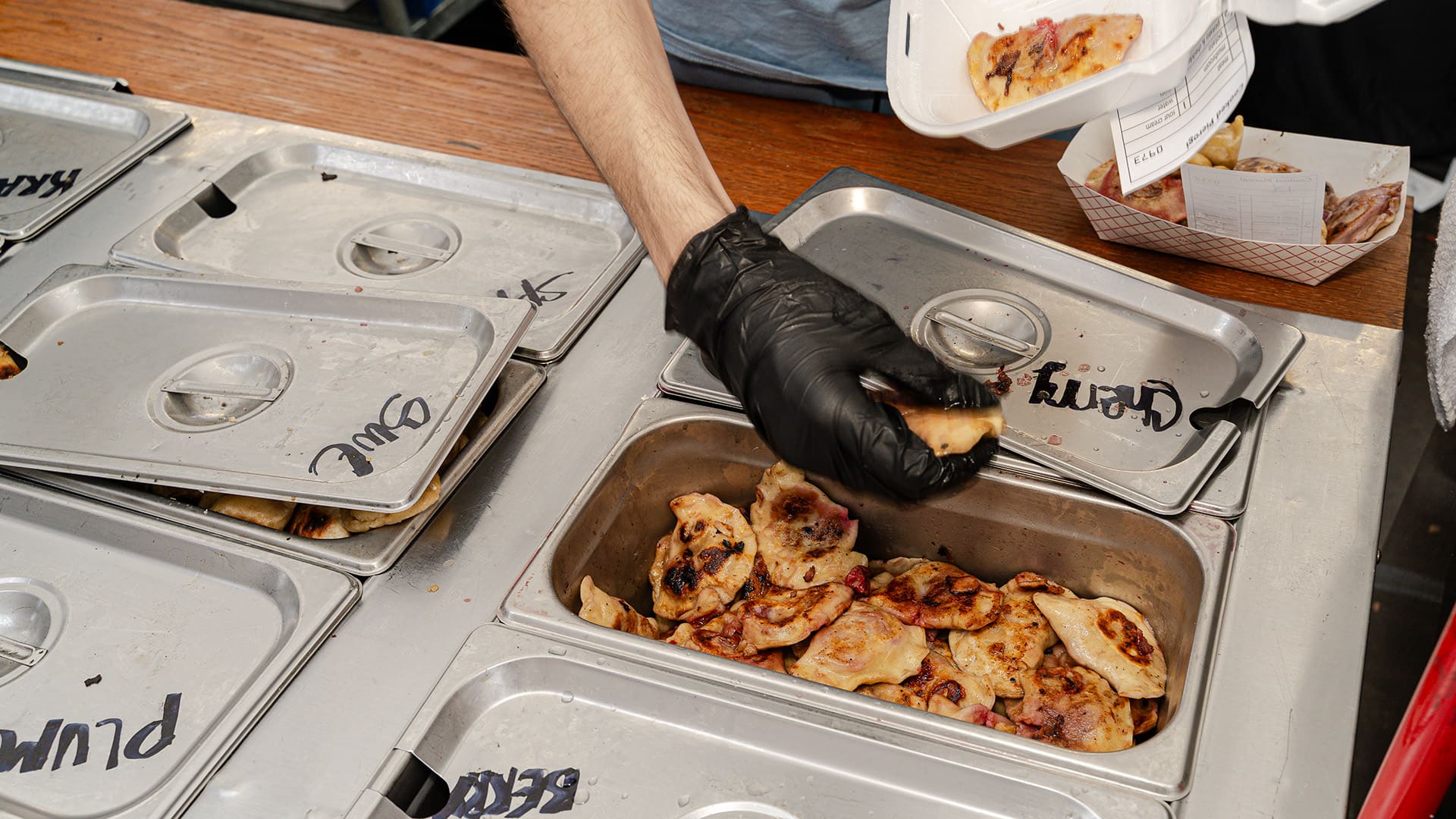 A worker wearing food service gloves takes pierogi out of a warming container