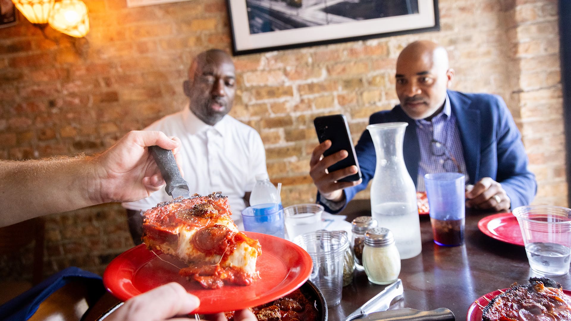 Two men take photos as a slice of pizza is cut and plated
