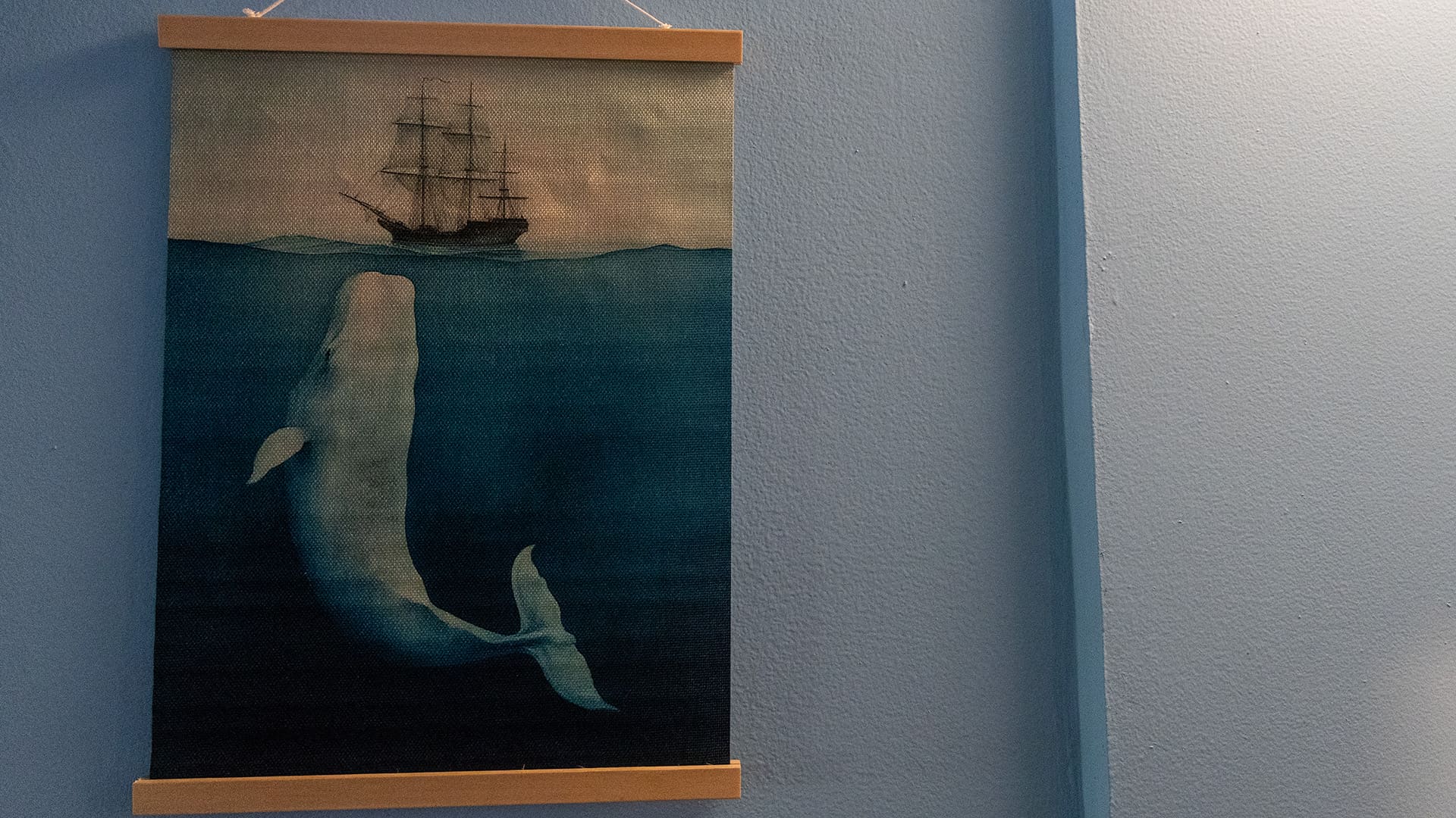 An artwork of a white whale under a sailing ship hangs on a wall