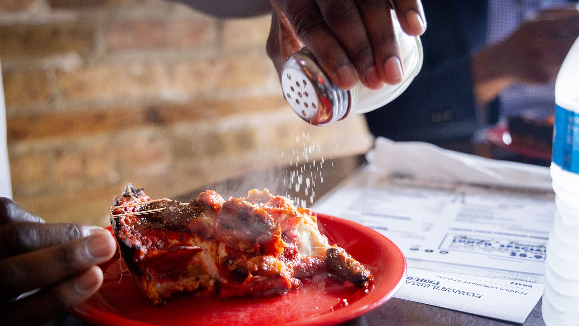 A hand sprinkles cheese on a slice of pizza