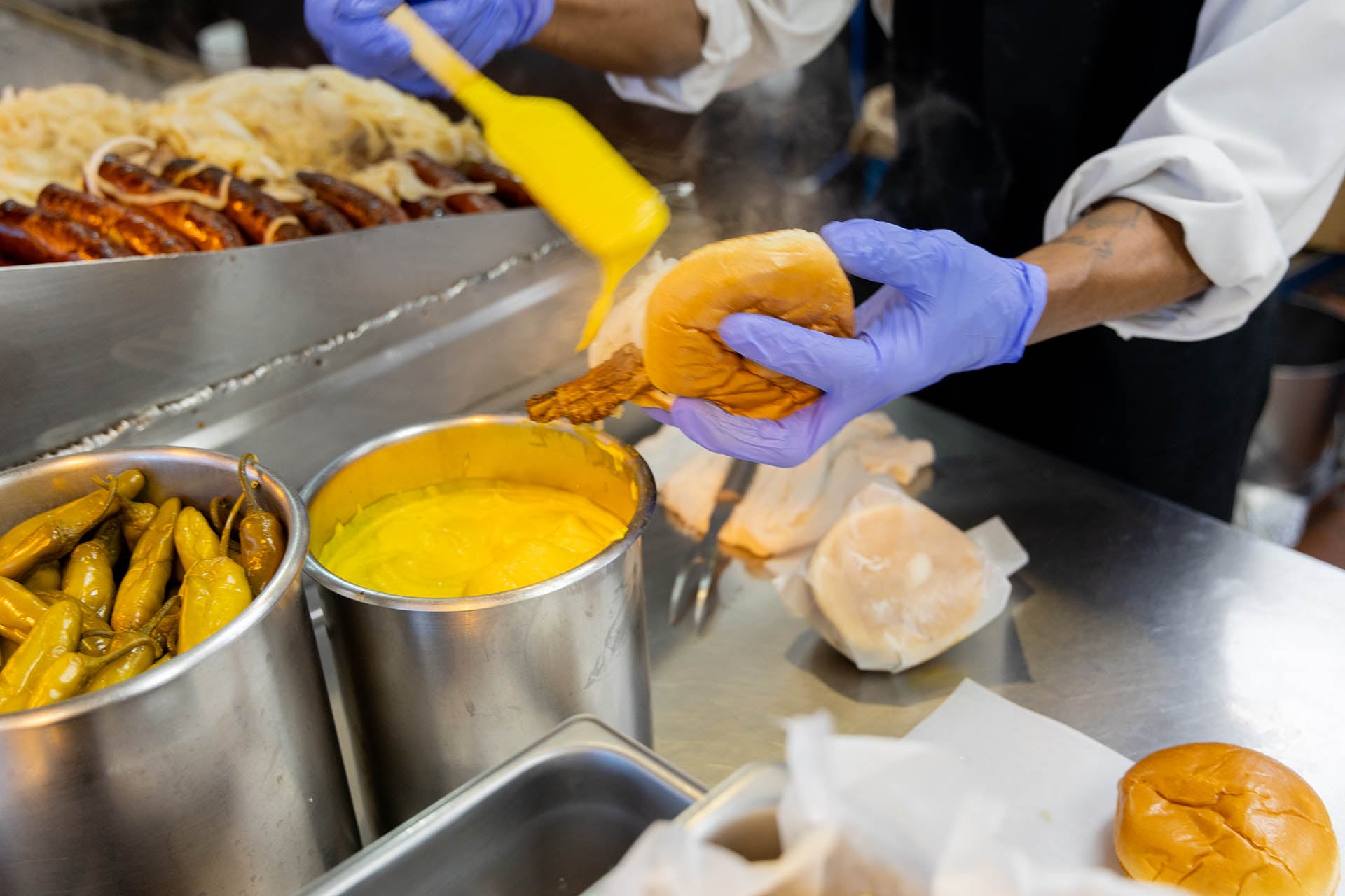 Worker brushing mustard onto a pork chop sandwich behind the counter at Jim’s Original