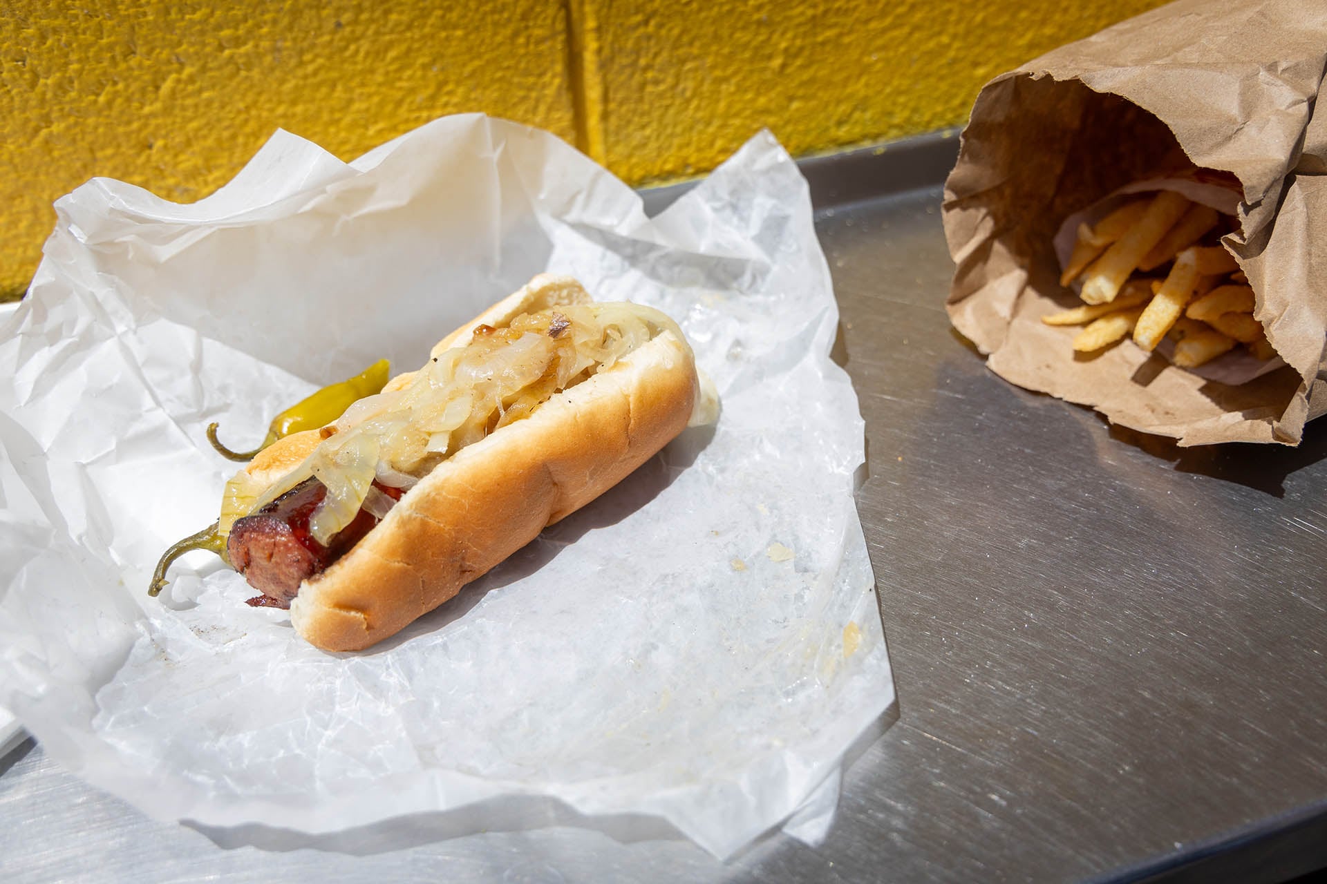 A Maxwell Street Polish with grilled onions and a sport pepper, with a bag of fries