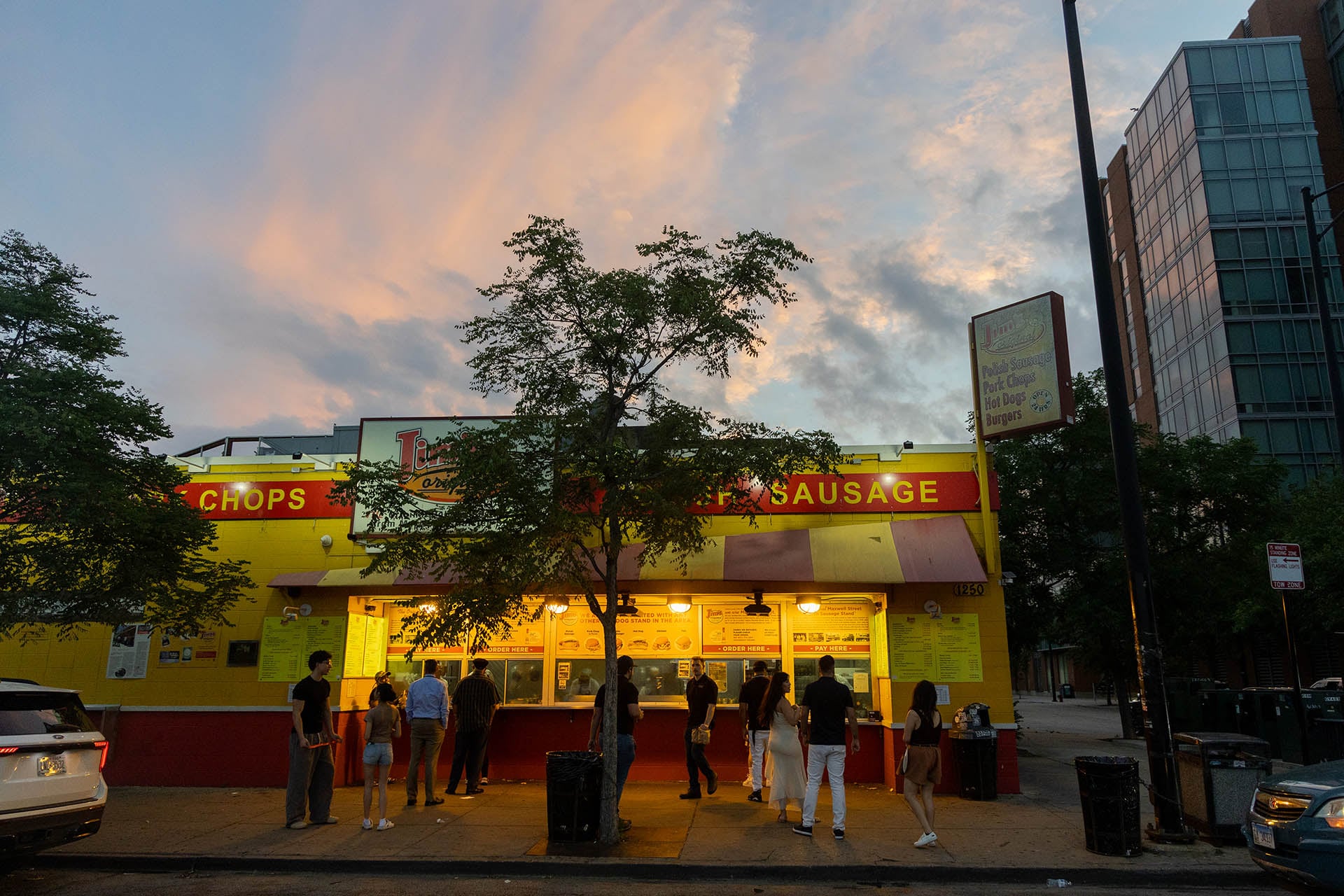Customers at Jim’s Original at dusk, with new residential buildings rising behind it
