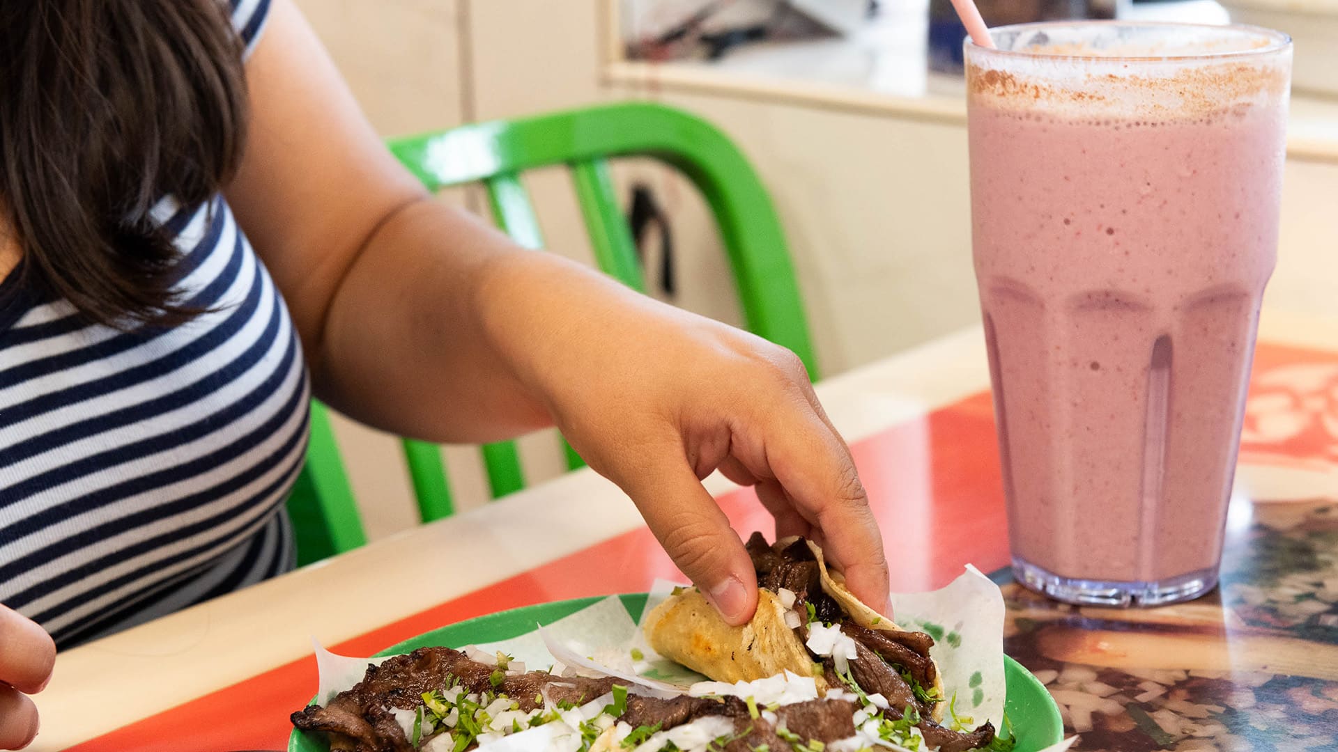 A hand reaches for a taco on a plate on a table next to a big pink smoothie