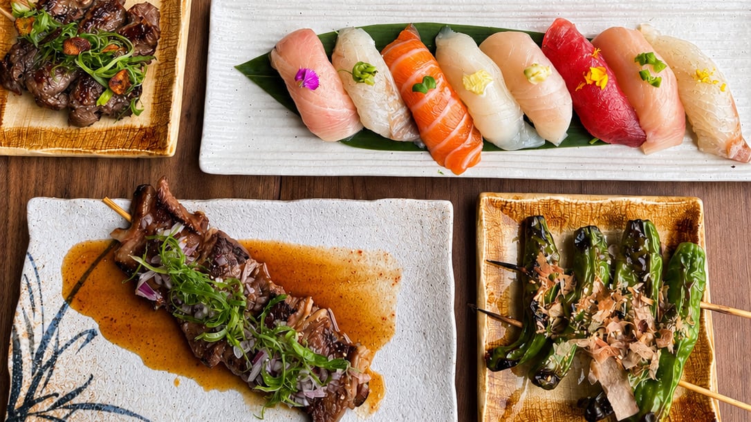 Plates of sushi and grilled skewers seen arranged on a table from above