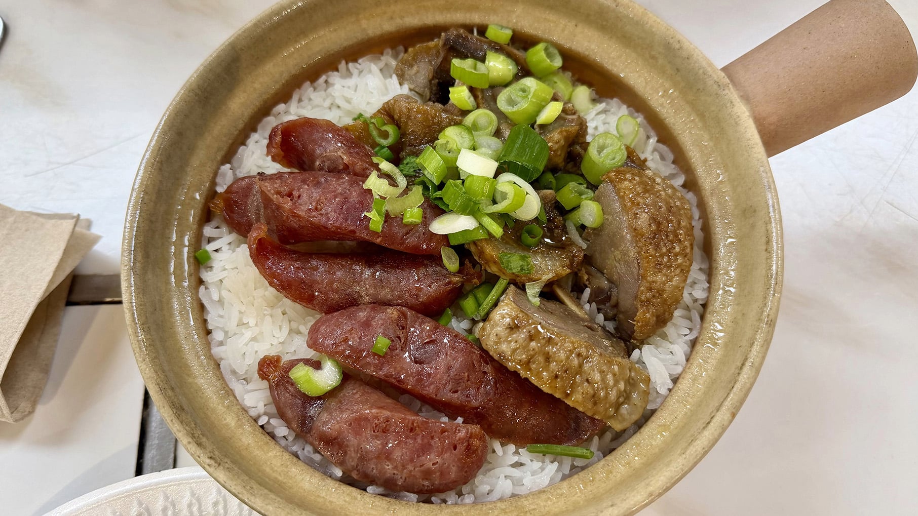 A claypot of rice topped with sausage and duck and scallions