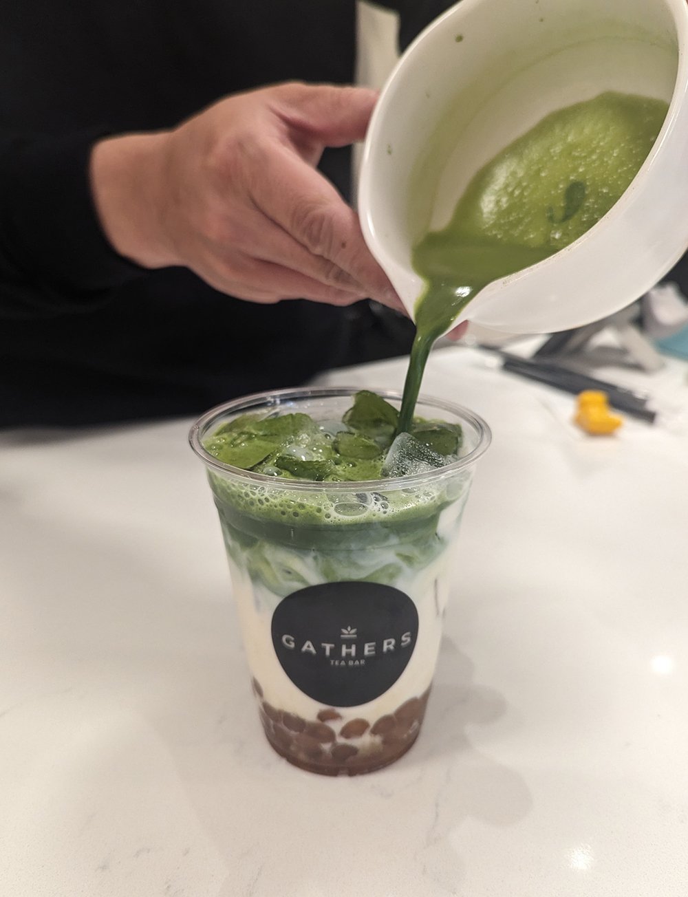 Hands pouring matcha into a plastic boba tea cup