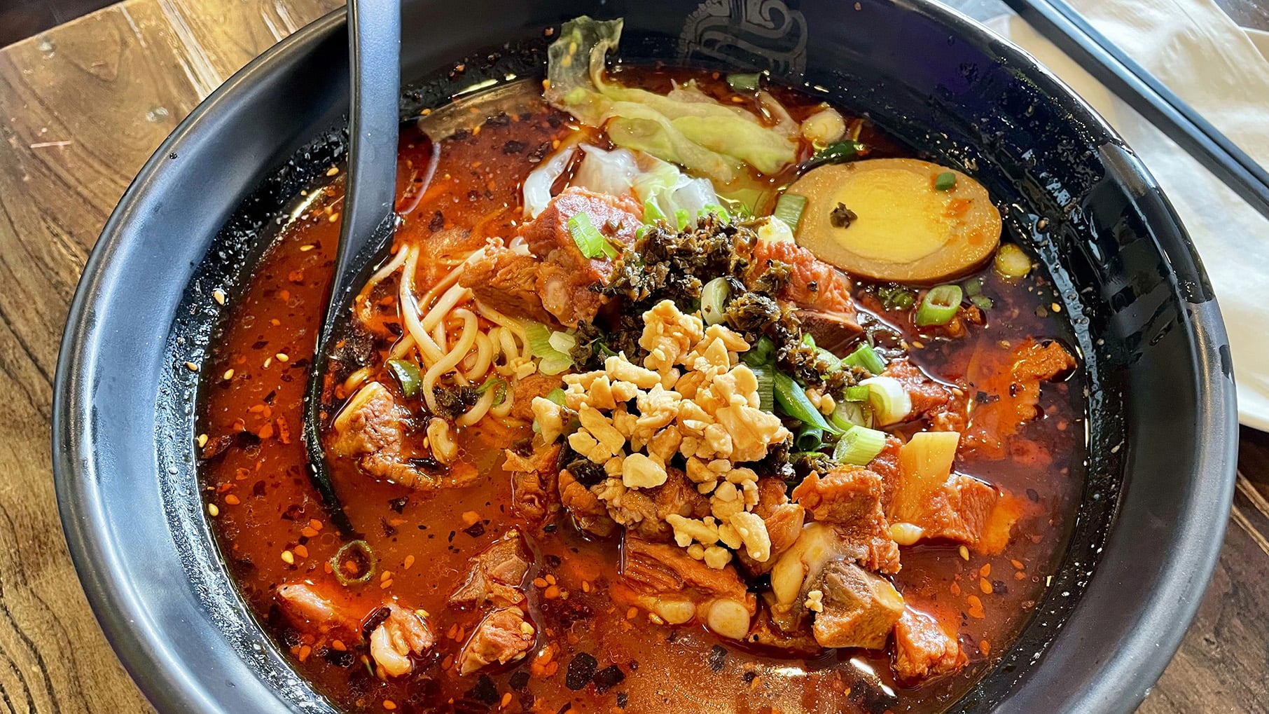 A bowl filled with noodles in broth, hard boiled egg, greens, red oil, and more