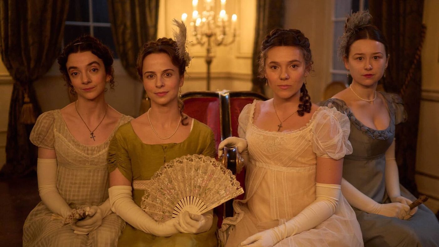 Four women sit and pose, one with a fan