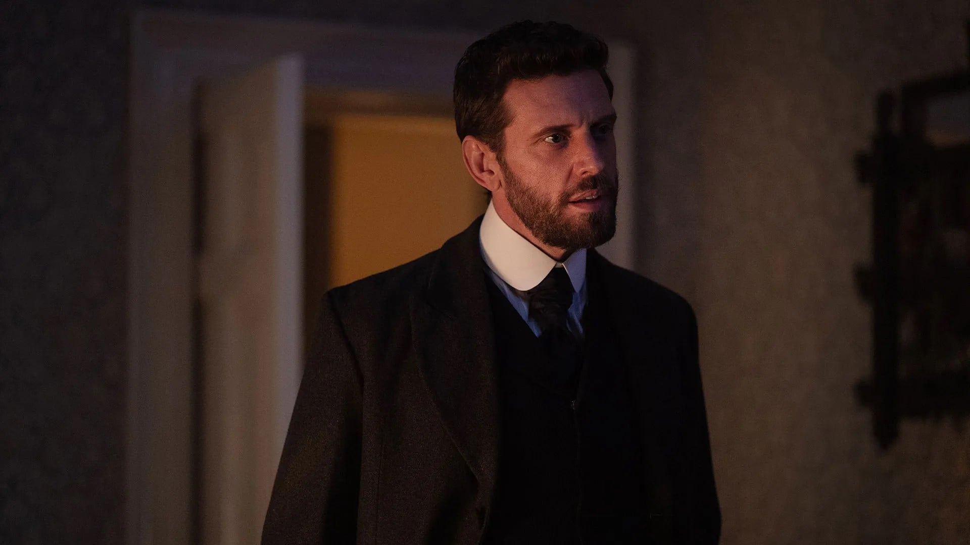 Alexander stands in a dark room in a suit