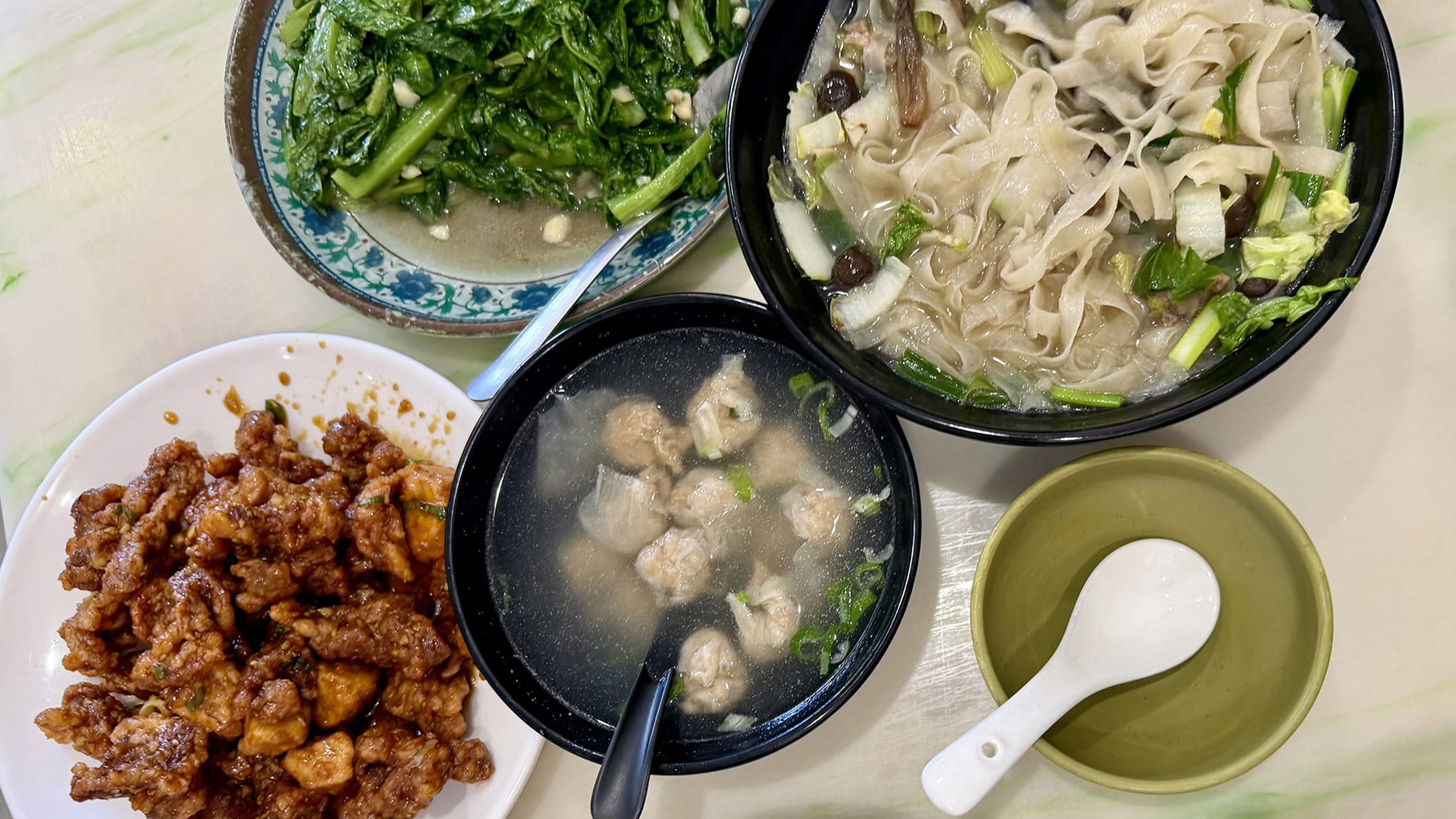 Plates and bowls of pork, greens, meatballs in broth, and noodles