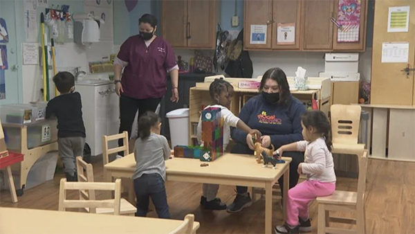 (WTTW News) Four children and two adults in a preschool classroom, playing around a table