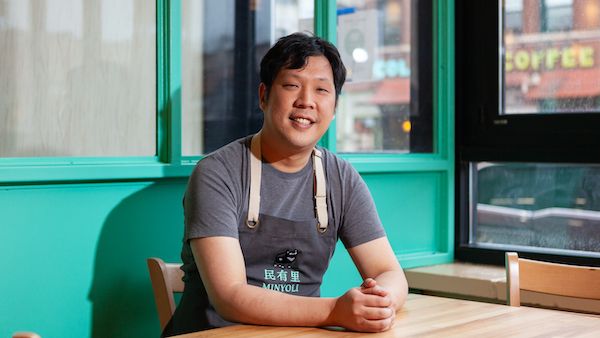 A seated Rich Wang smiles in front of a seafoam green backdrop and windows
