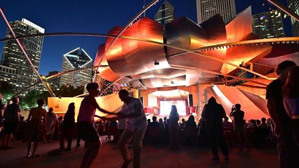 People dancing at night on the lawn in front of the Pritzker Pavilion 