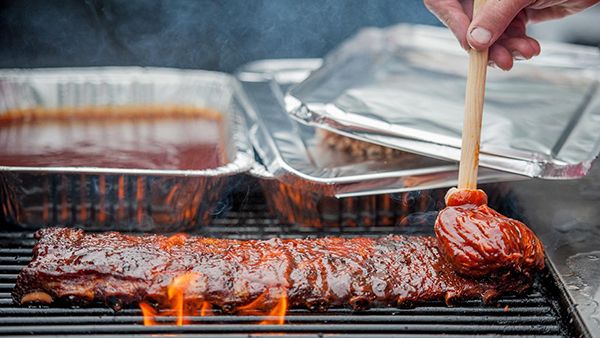 Ribs being glazed with BBQ sauce on a grill