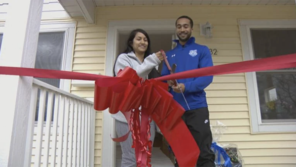 Tanais Valdillez and Steven Wells stand on their front porch with giant scissors and cut a giant red ribbon